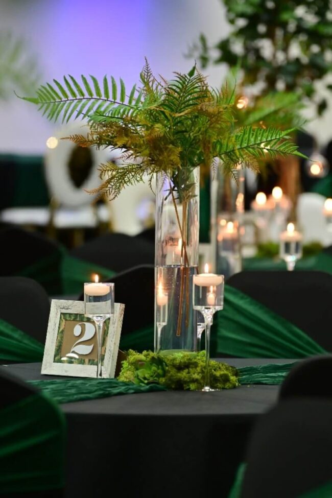 Centerpieces with trees featuring tall vases, greenery, and floating candles for elegant party table styling.