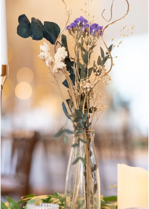 Glass bottle with dried flowers and greenery used as elegant event decor centrepiece.