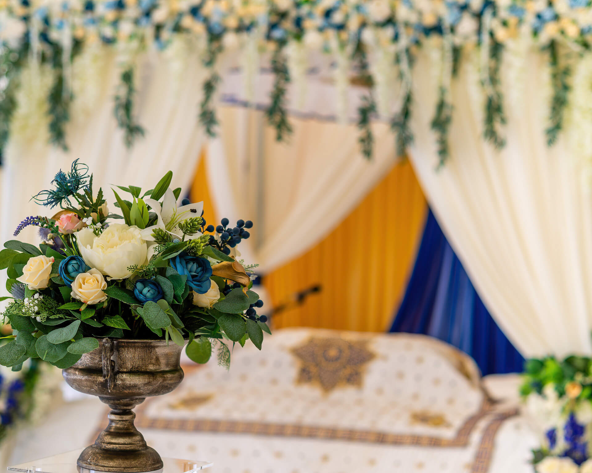 Blue and white floral display in front of a draped canopy backdrop