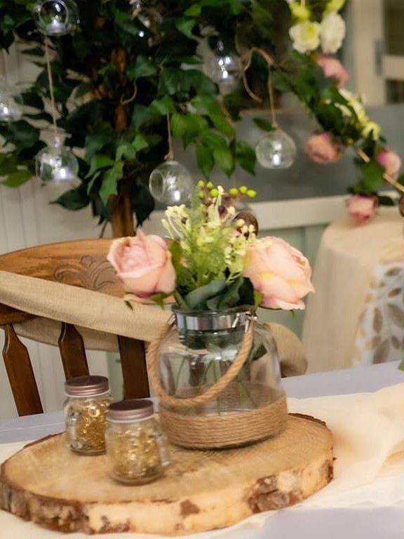 Decorative mason jars beside a floral arrangement on a wooden table slice