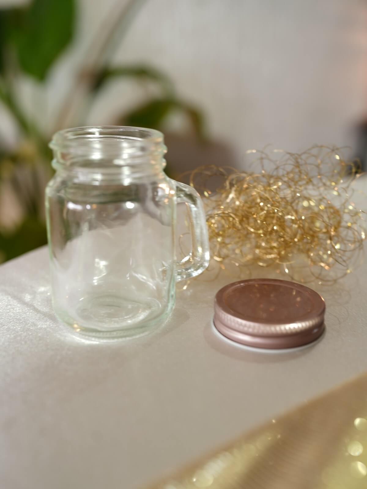 Clear mason jar with handle and removable metal lid beside decorative lights