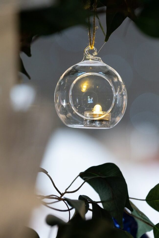 Hanging tealight holder suspended from greenery with candlelight inside