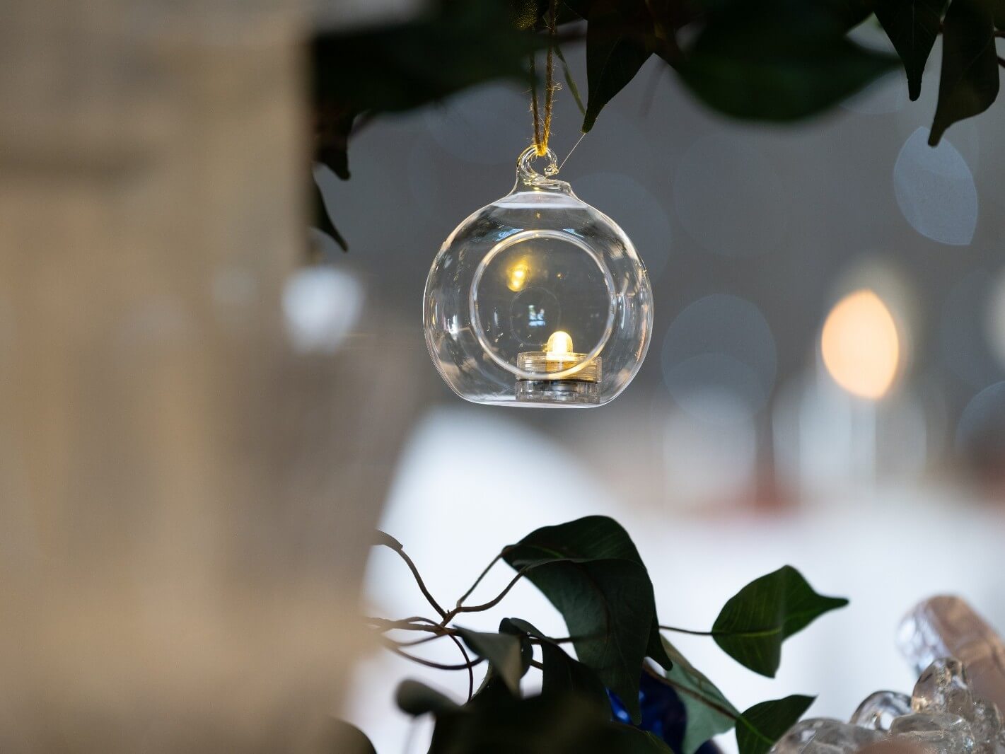 Hanging tealight holder suspended from greenery with candlelight inside
