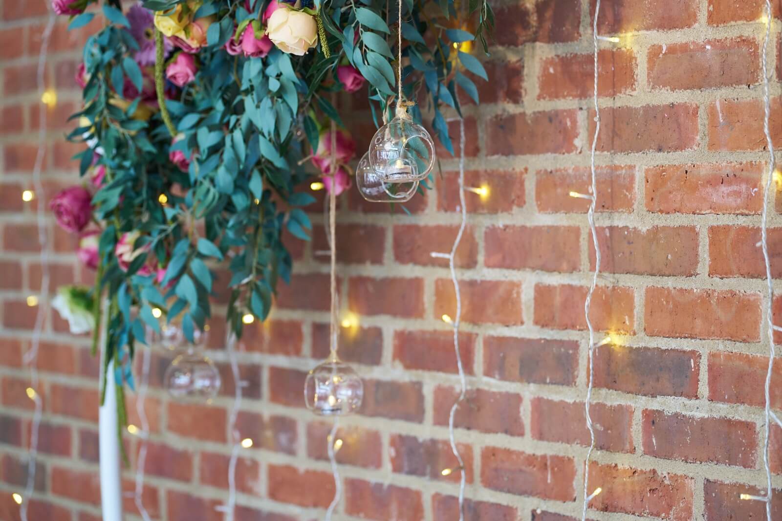Hanging tealight holders suspended beneath flowers and greenery
