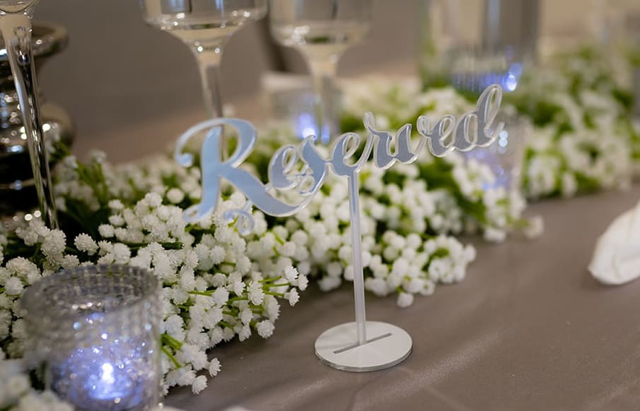 Room dressing with a reserved table sign surrounded by elegant white florals and candlelit décor.