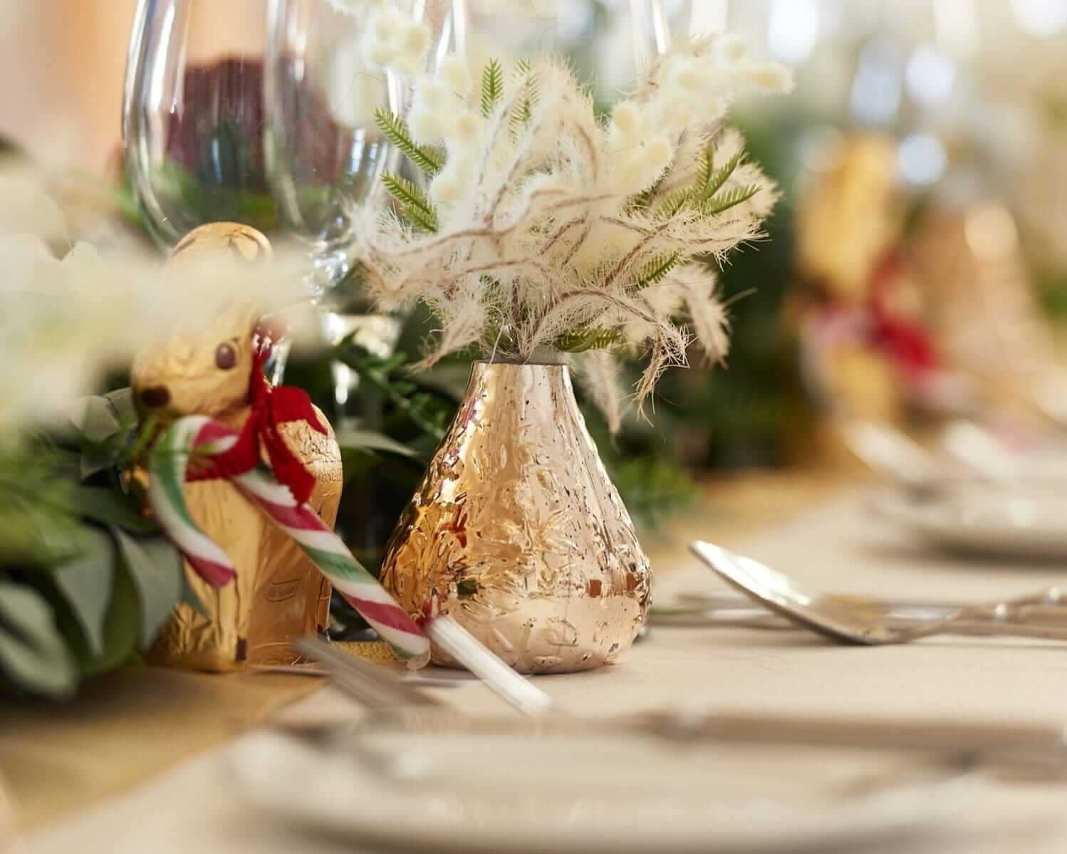 DIY venue styling with a gold bud vase, soft foliage and festive chocolate favour on a dressed table.