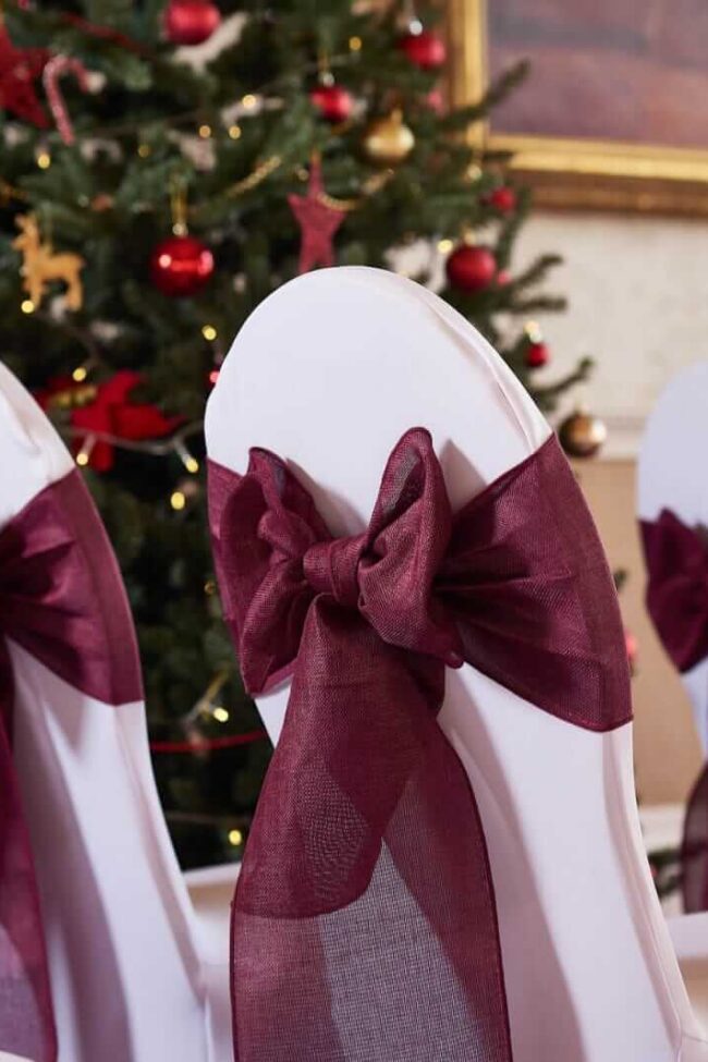 Red chair sashes in a burgundy shade on chair covers for a ceremony aisle setup