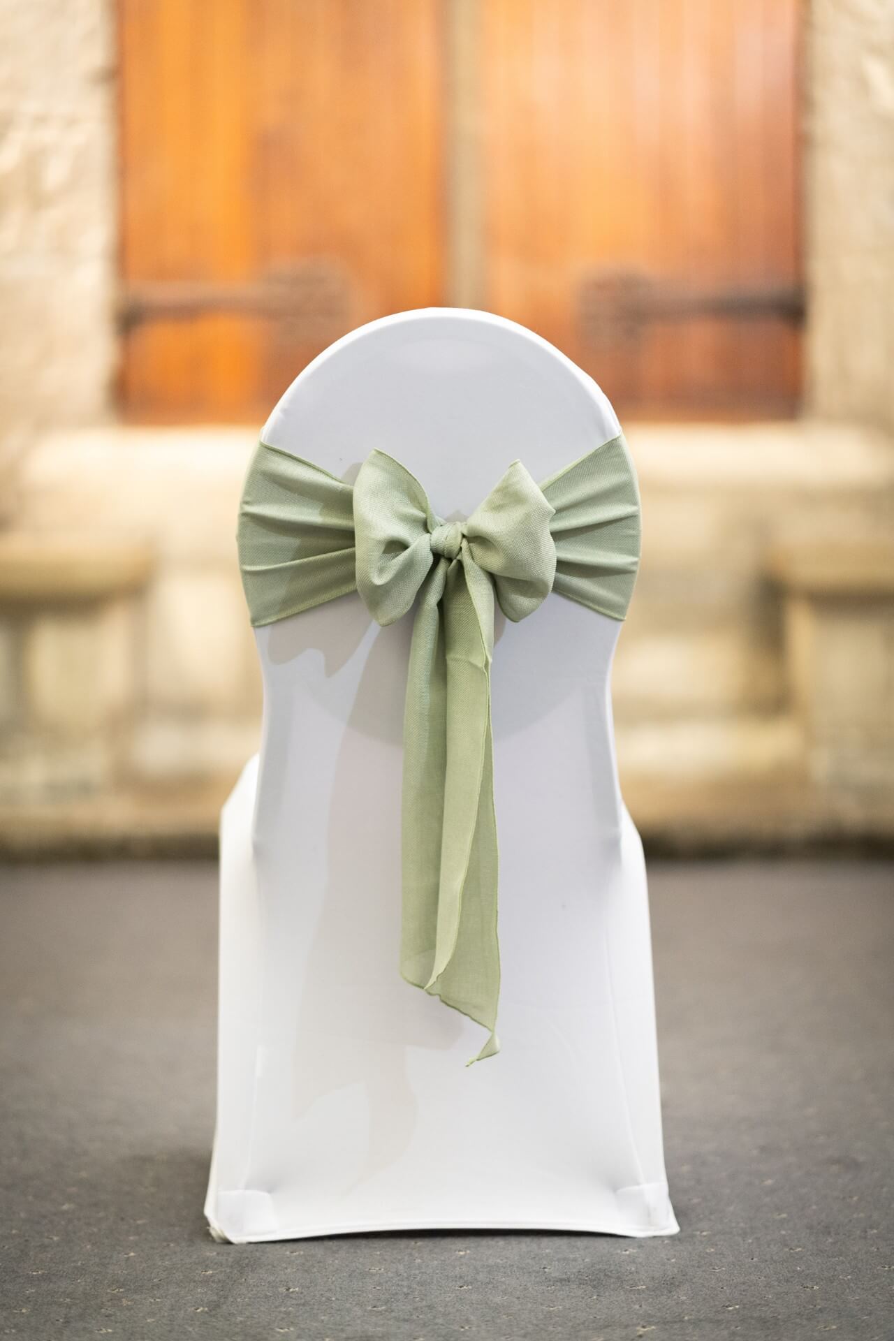 Front view of a white-covered chair with a sage burlap sash bow