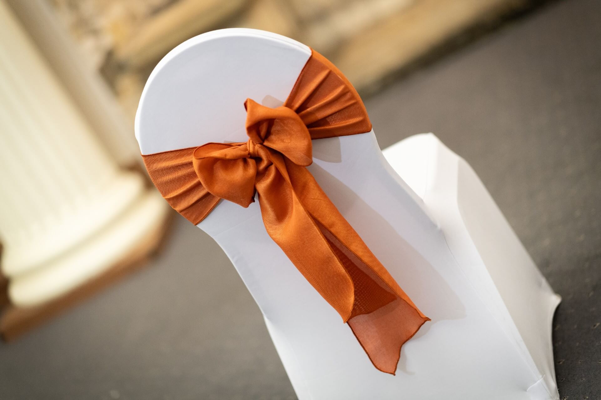 Terracotta sashes tied on a white chair cover for wedding chair sash hire