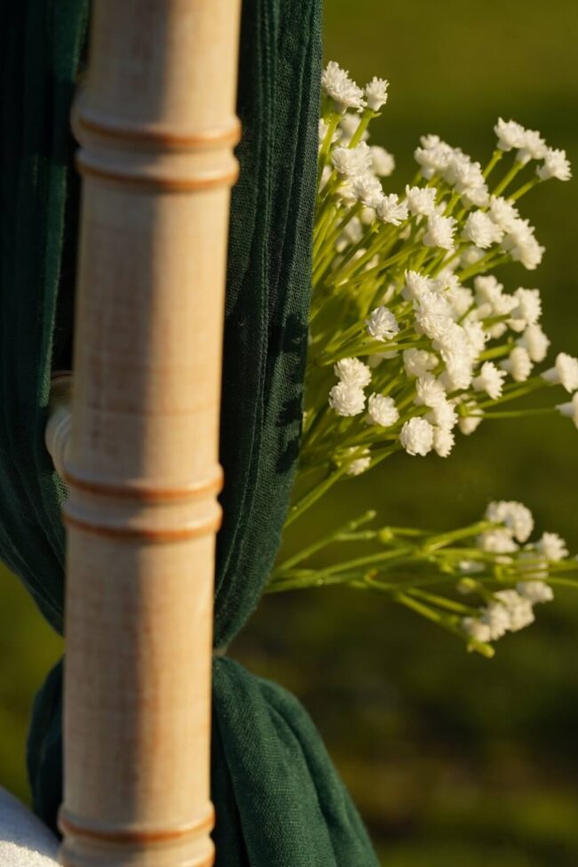 Green chair drapes in cheesecloth on a chiavari chair, tied with white floral detail.