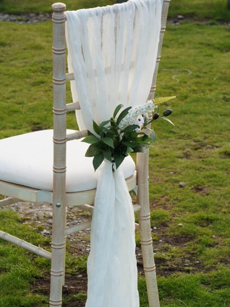 White cheesecloth drape styled on a chiavari chair with greenery detail