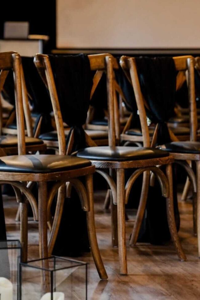 Rows of wooden chairs styled with black chiffon drapes in a ceremony layout