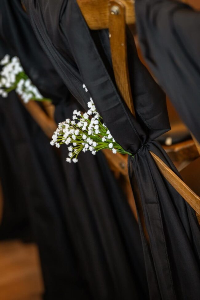 Wide view of ceremony chairs styled with black chiffon drapes