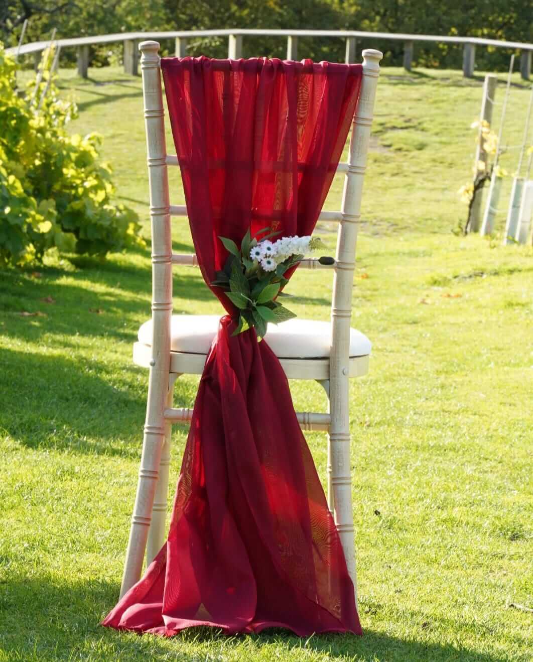 Red chiffon drape styled as a vertical drop on a chiavari chair with greenery detail