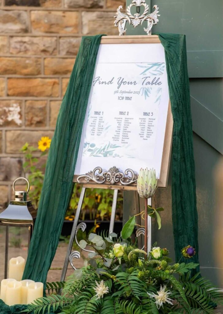 Antique easel stand in silver holding a seating plan sign with green drape