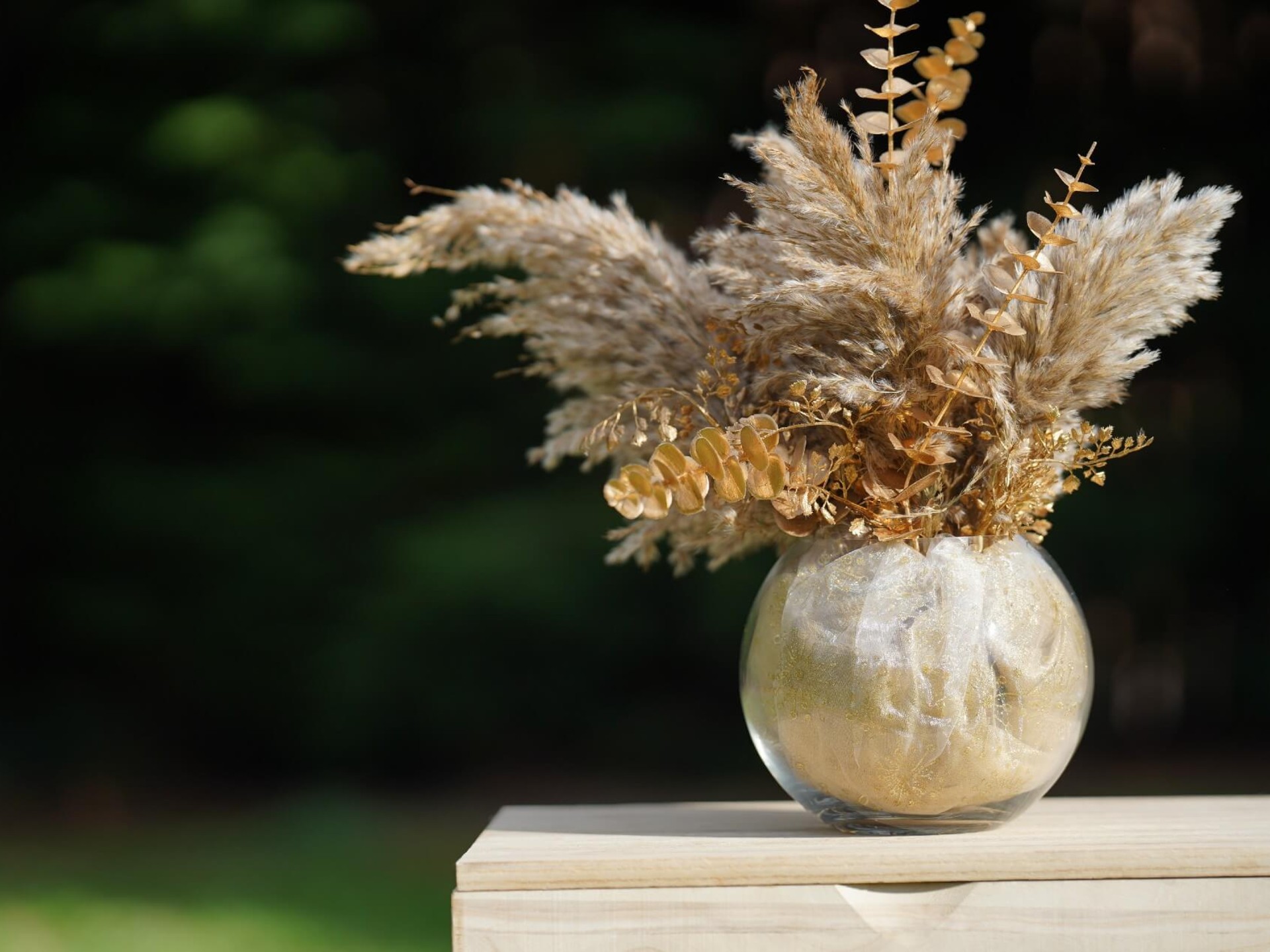 Clear glass fish bowl vase with rounded shape and dried floral display