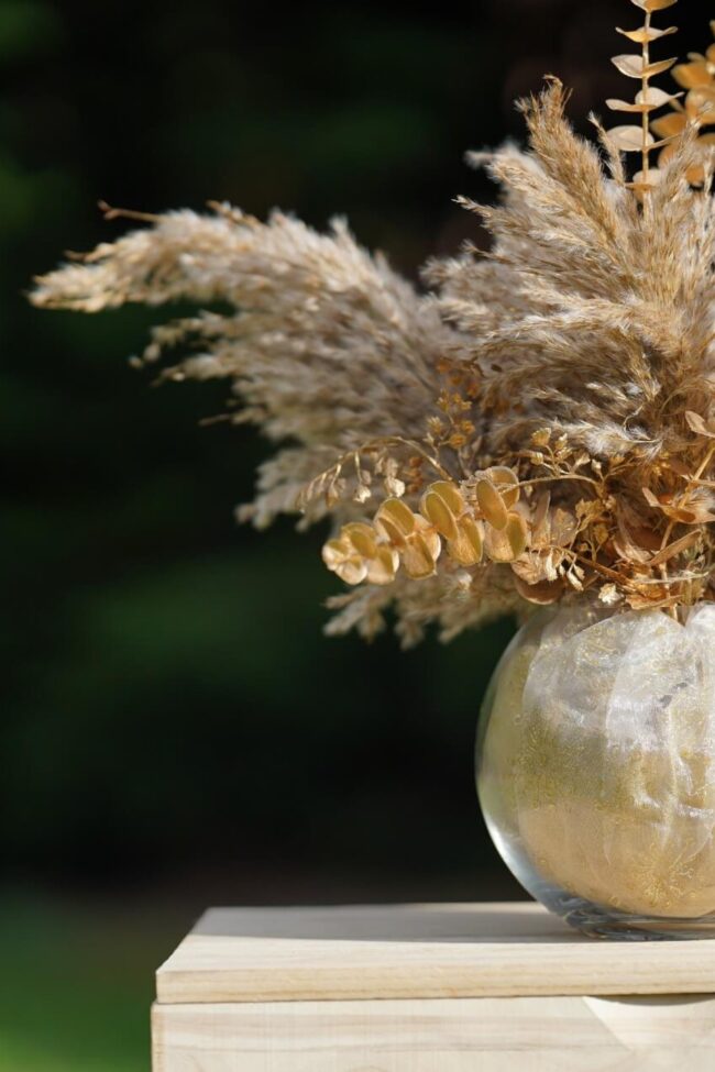 Elegant fish bowl centrepieces featuring pampas grass and dried foliage arranged in a round glass vase for a natural boho look.