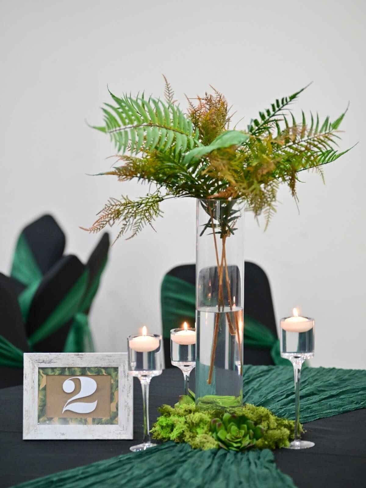 Three clear glass floating candlesticks arranged around a greenery display