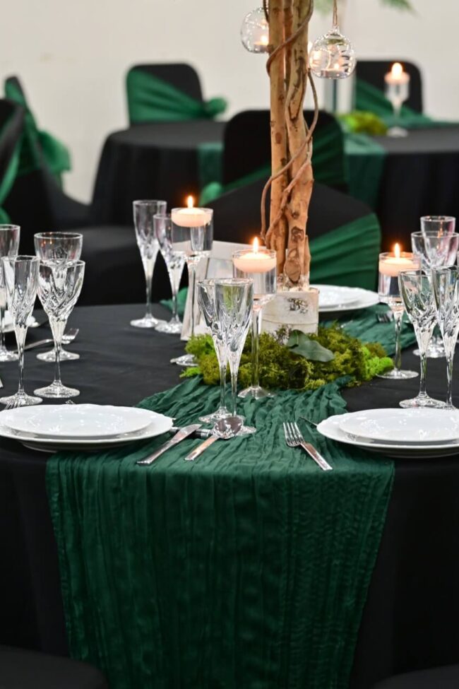 Green cheesecloth table runner styled on a round event table with candles and glassware