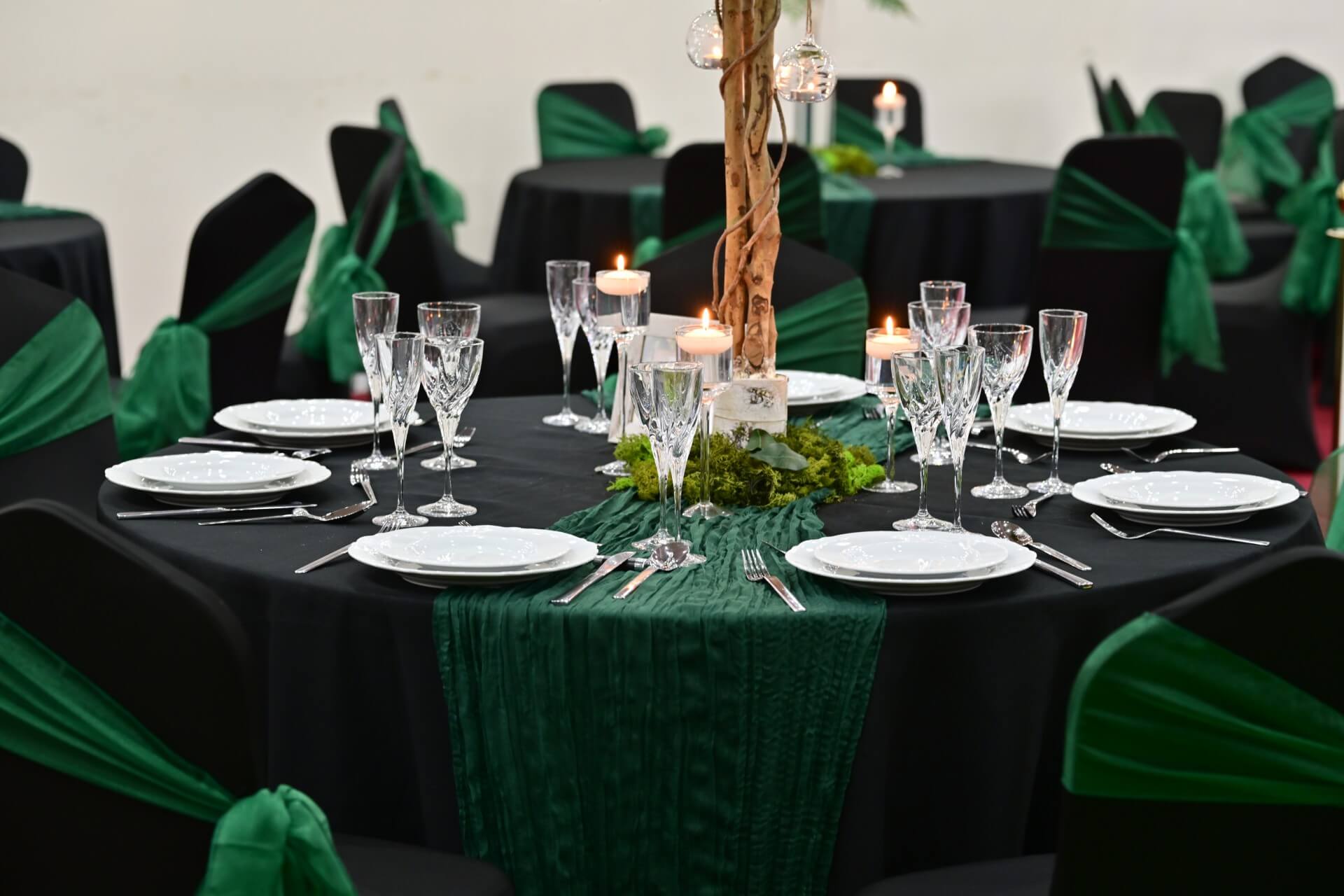 Green cheesecloth table runner styled on a round event table with candles and glassware