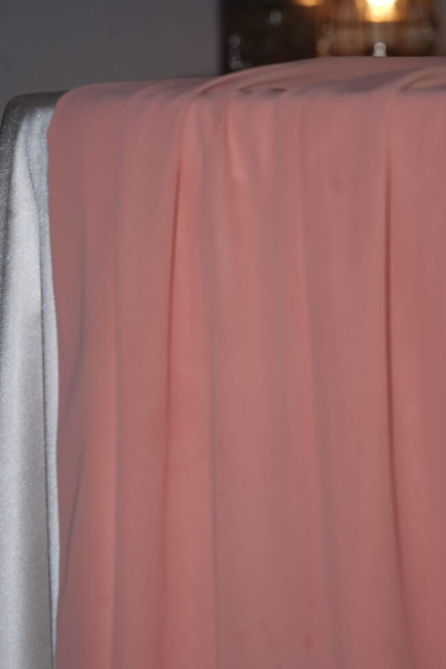 Pink table runner in chiffon fabric draped over the edge of a dressed table