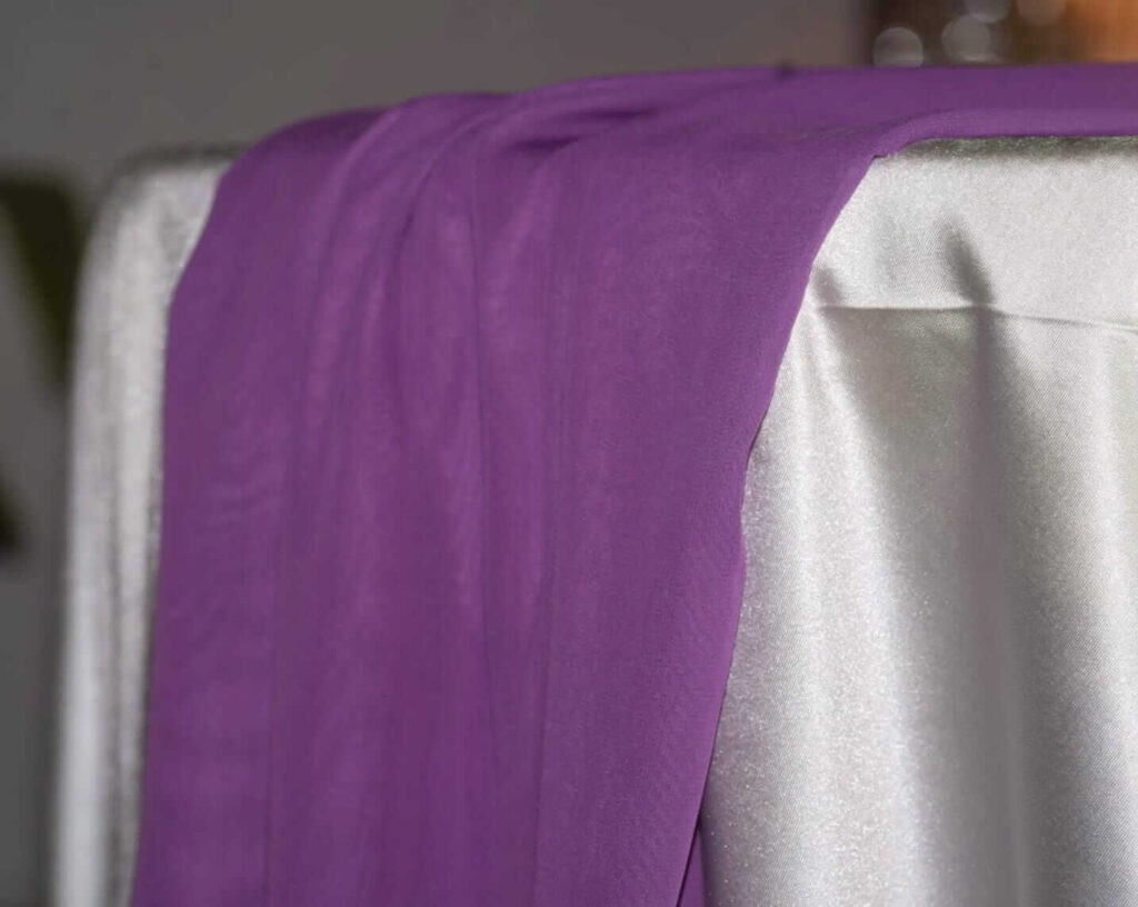 Purple table runners in chiffon fabric draped over the edge of a dressed table
