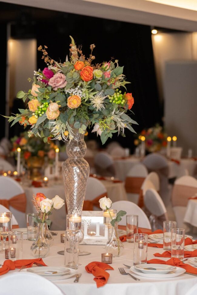 Tall artificial flower centrepiece on a tall glass vase styled for event table