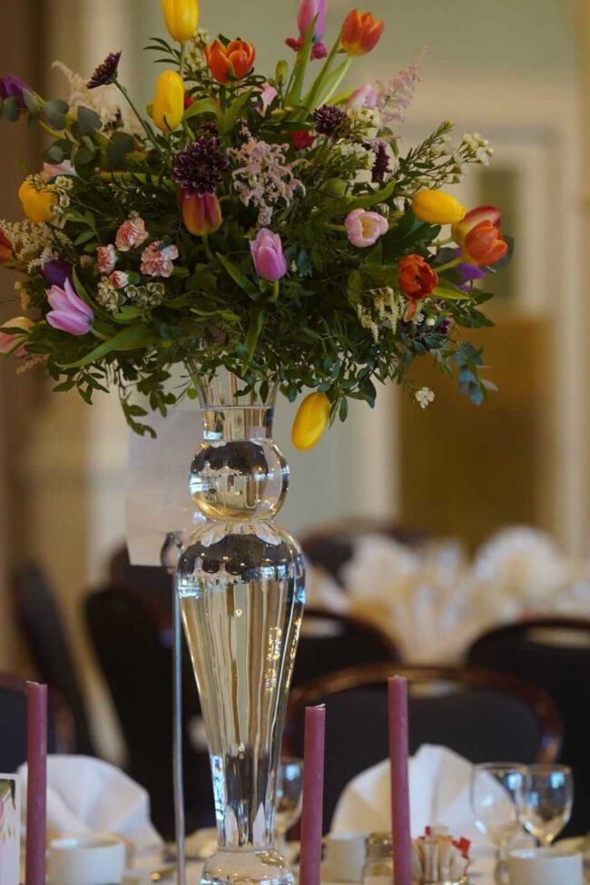 Fresh floral centrepieces with seasonal blooms and greenery on a tall glass vase