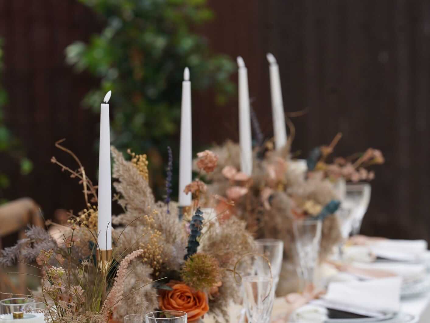 Clear fish bowl vase styled with flowers and tall candles on a long table
