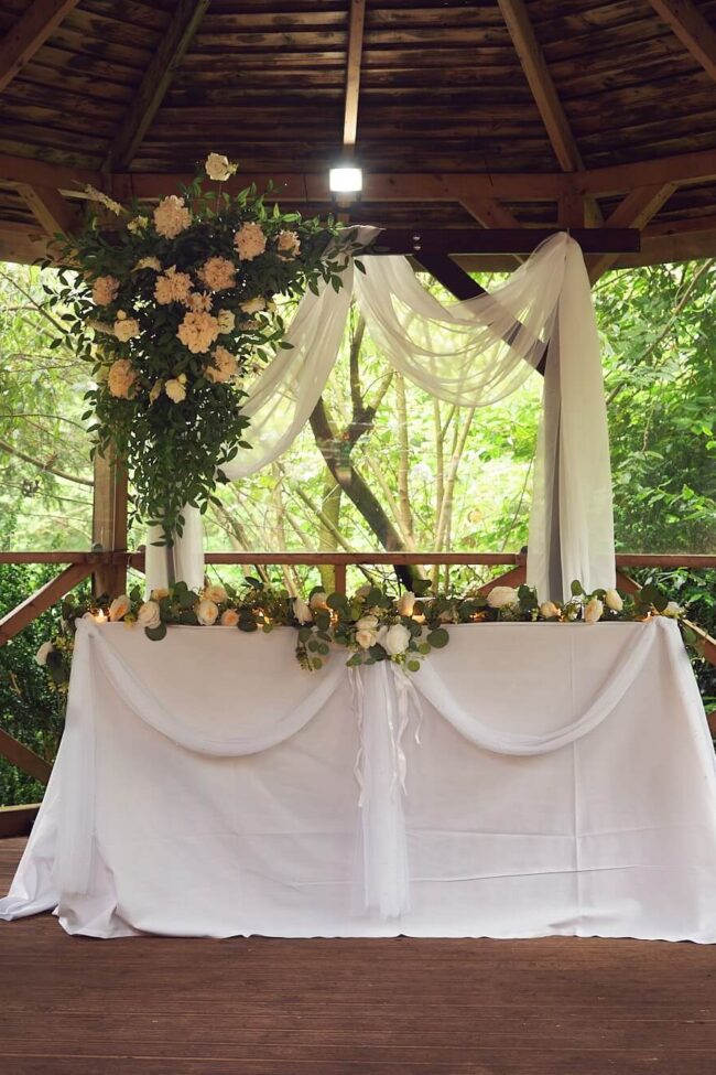 Wooden arch hire with white draping and cream flower arrangement