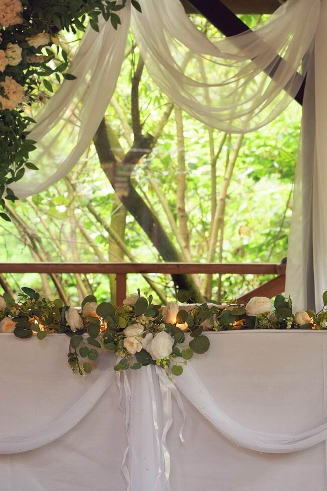 Wooden archway decorated with cream flowers and white fabric