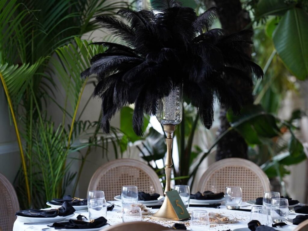 Black feather centrepiece on a tall gold stand above a white dining table