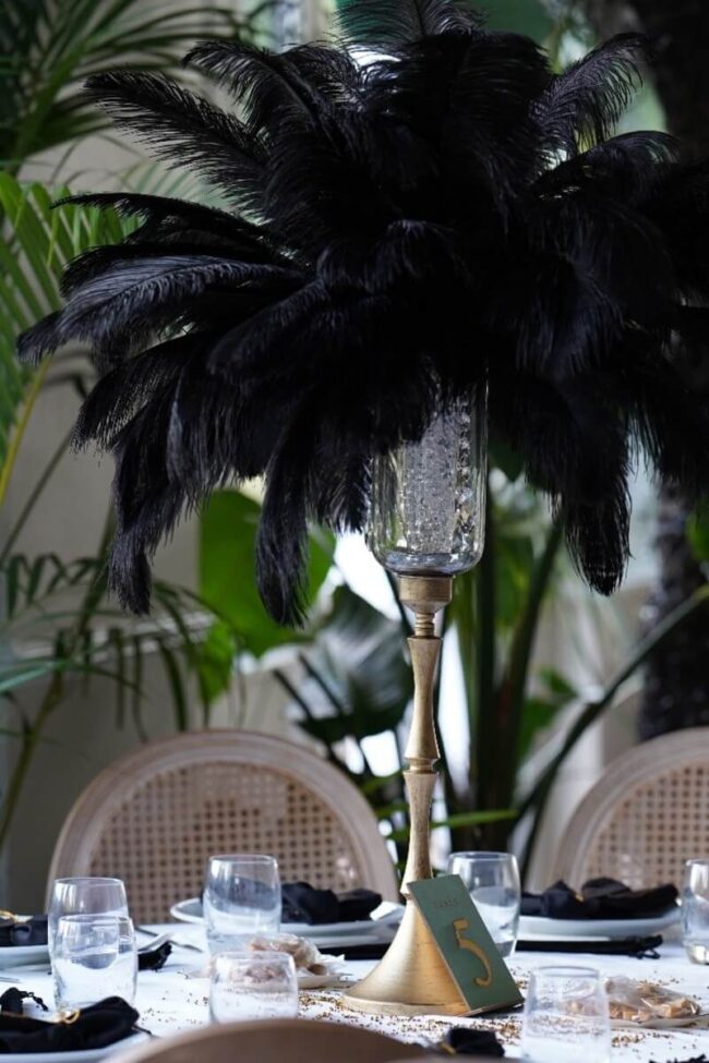 Black feather centrepiece on a tall gold stand above a white dining table