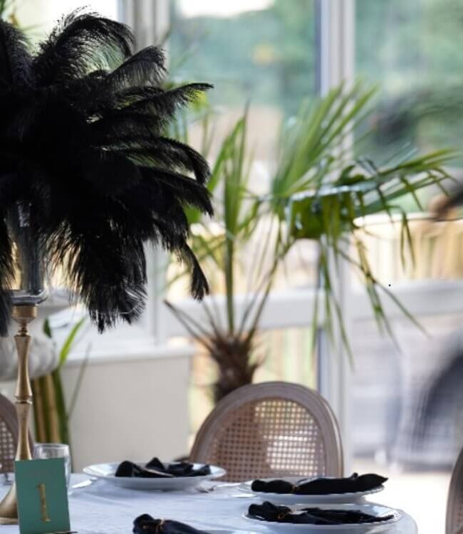 Black feather centrepiece above a white table with black place-setting details