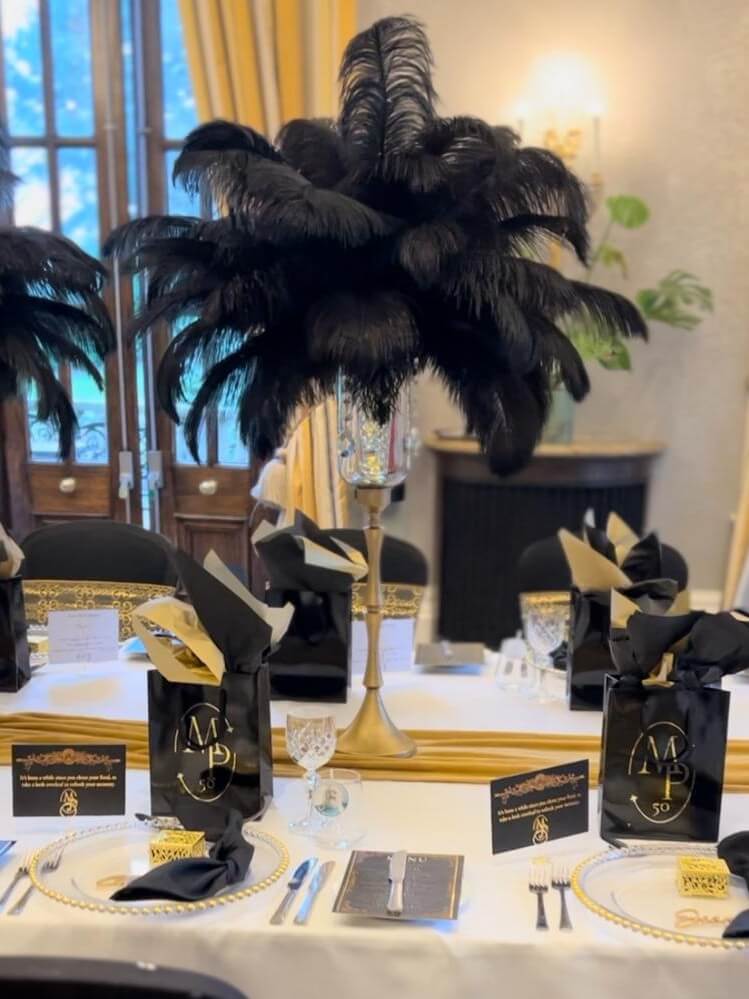 Tall black feather arrangement above a black, white and gold celebration table
