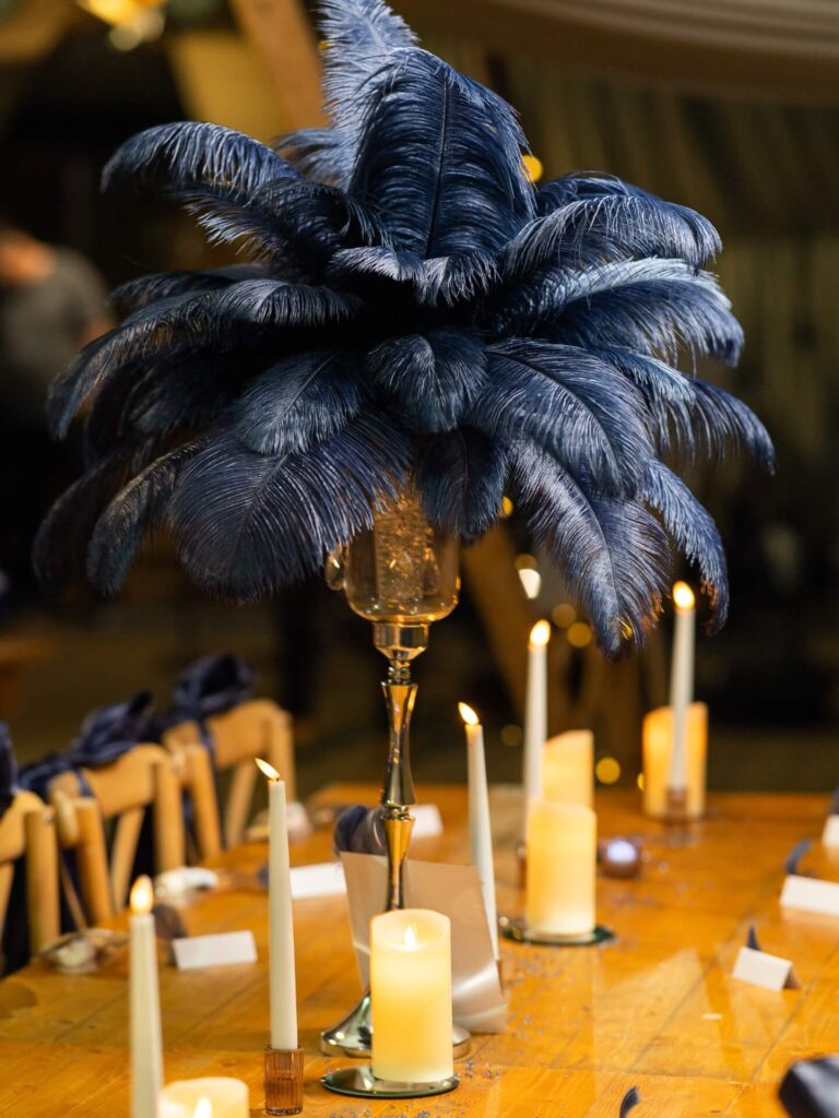 Navy blue feather centrepiece on a tall stand surrounded by candlelight