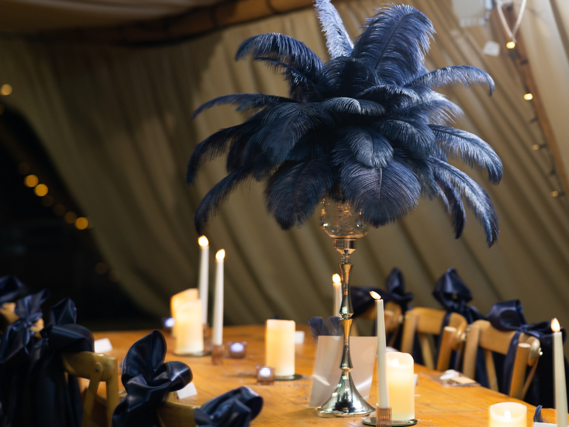 Navy ostrich feather centrepiece on a tall silver stand at a candlelit dinner table