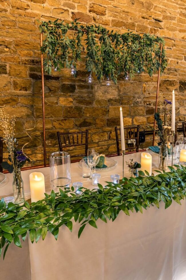Copper frame arch with foliage positioned behind a decorated top table