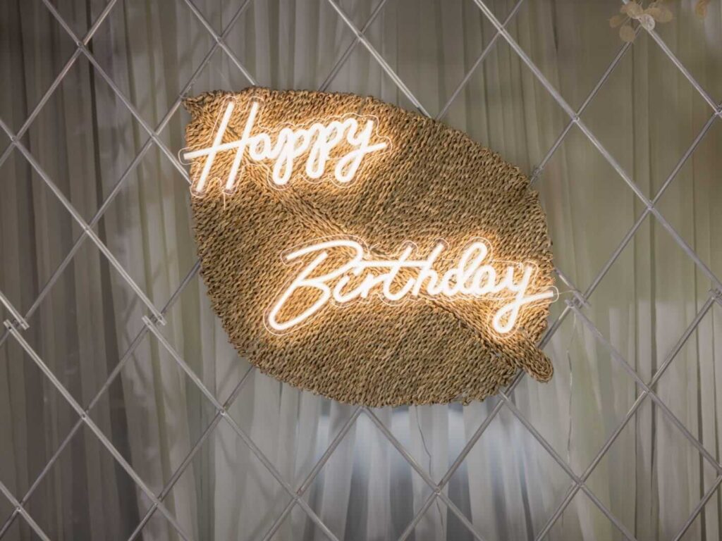 happy birthday sign for hire on a woven leaf backdrop