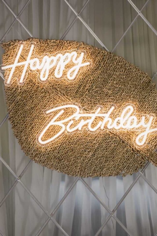 happy birthday sign for hire on a woven leaf backdrop