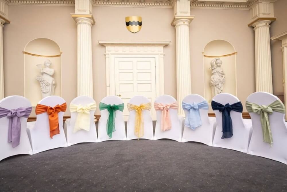 Colourful chair sashes on white chair covers displayed for chair decor hire.