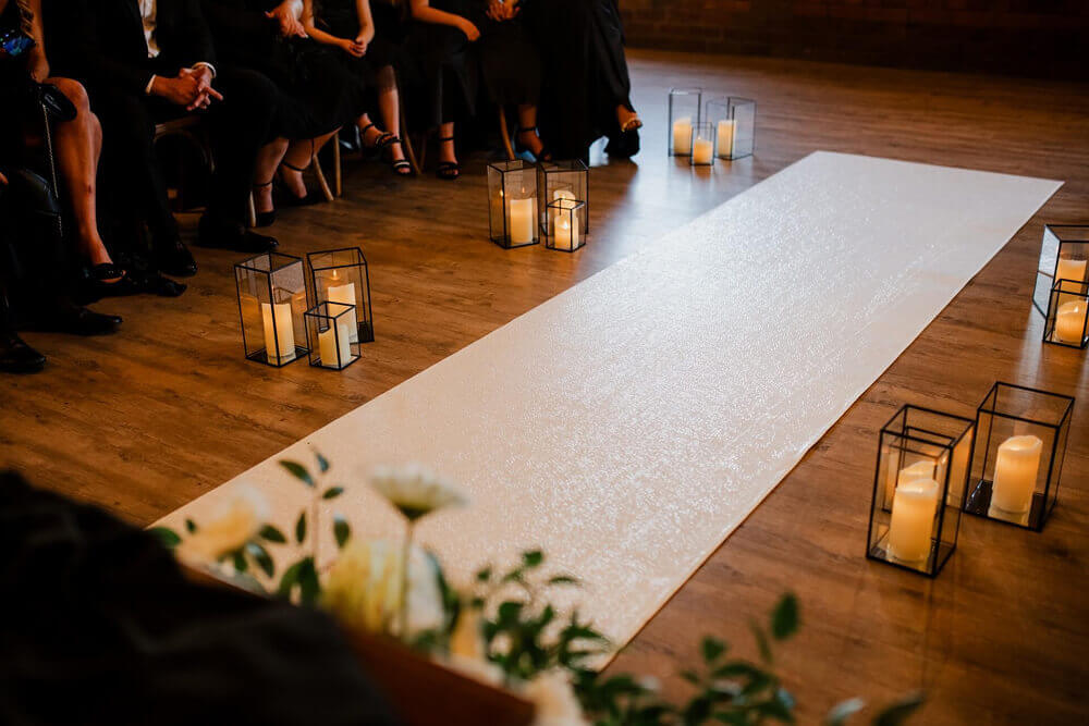 Elegant candlesticks and candle lanterns lining a white wedding aisle runner for a romantic ceremony setup.