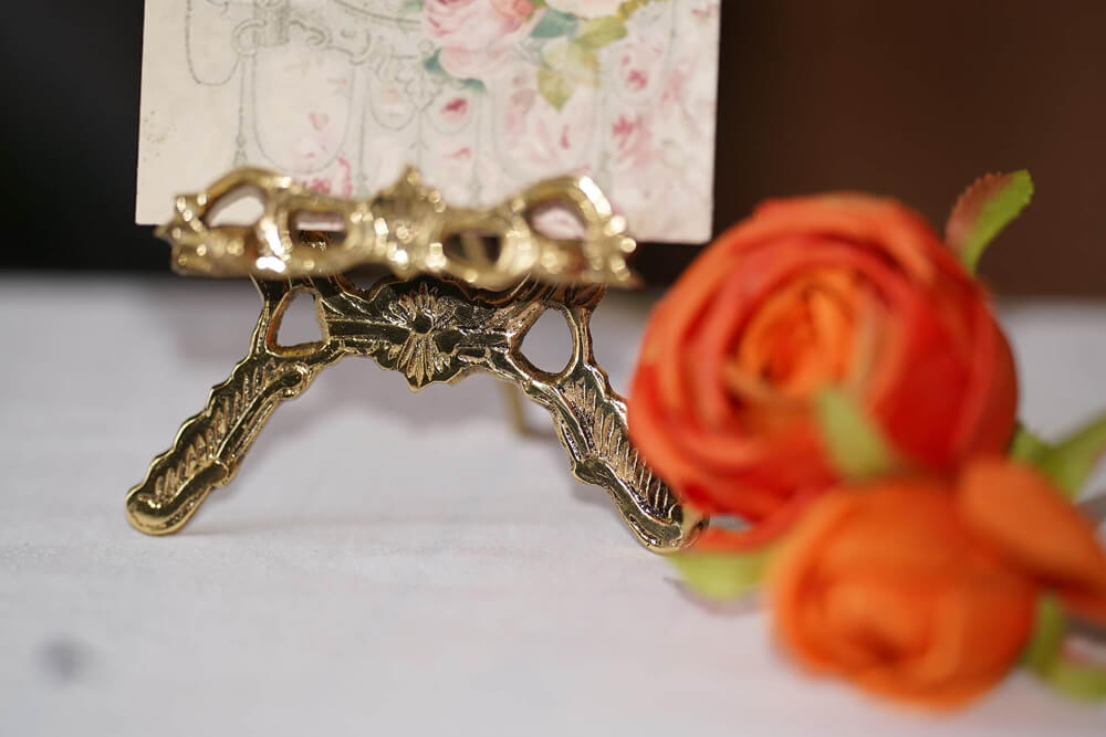 Close-up of a decorative gold mini easel holding a floral sign with orange roses, perfect for wedding easels and signs décor.