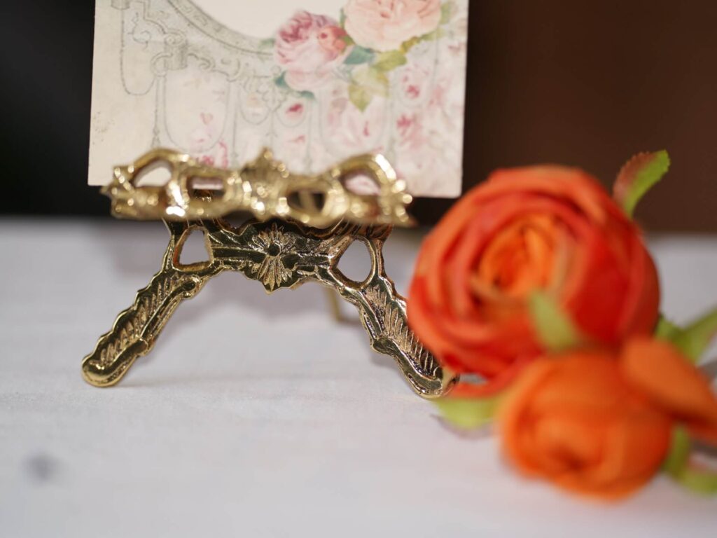 Gold decorative easel displaying a floral sign with orange roses, ideal for elegant wedding signs and easels styling.