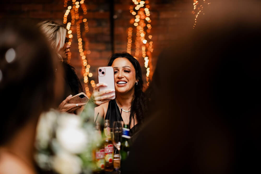Guest smiling and taking a photo at an event with glowing festival lights in the background.