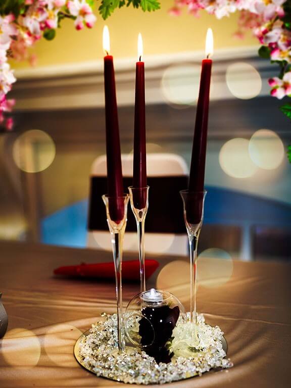 Elegant table centrepiece with tall burgundy candles and crystals, styled as part of our party packages.