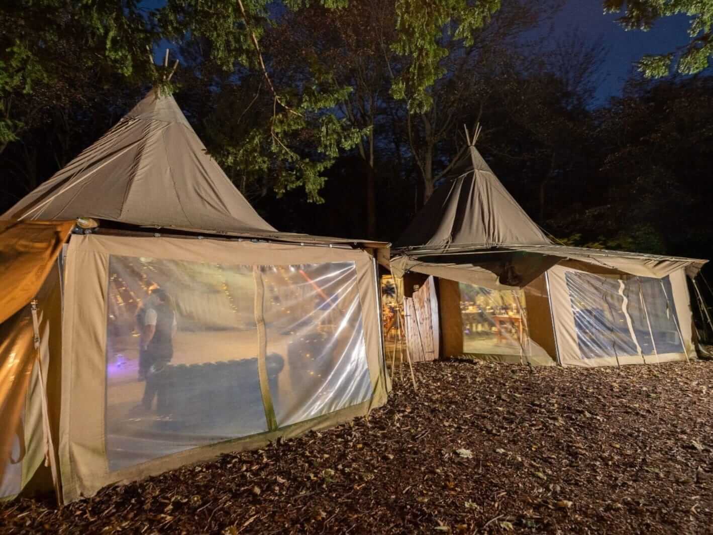 Large outdoor tipi tents lit at night, styled for themed events in a woodland setting.