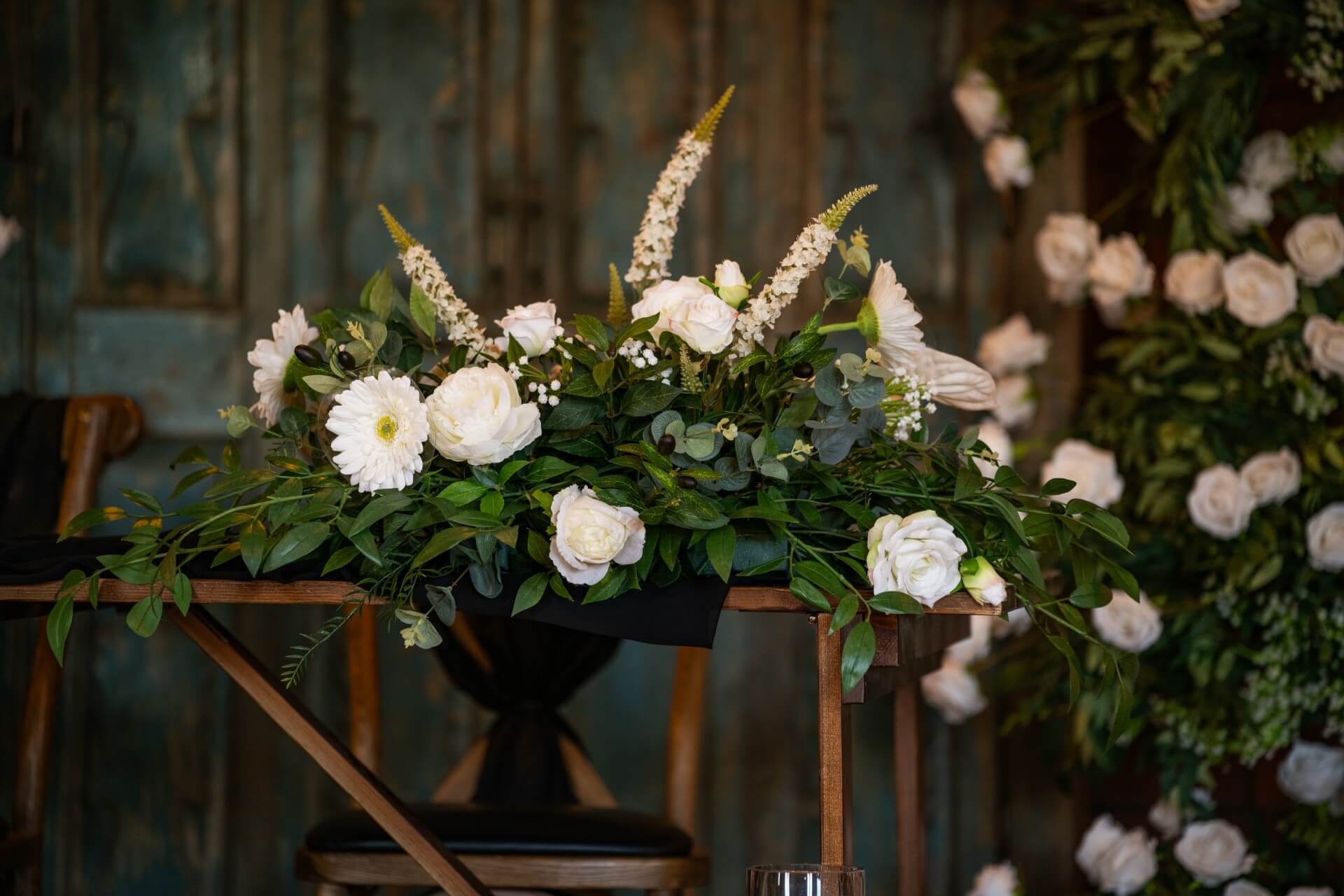 Elegant white rose floral display with lush foliage arranged as part of a greenery archway for a wedding ceremony.