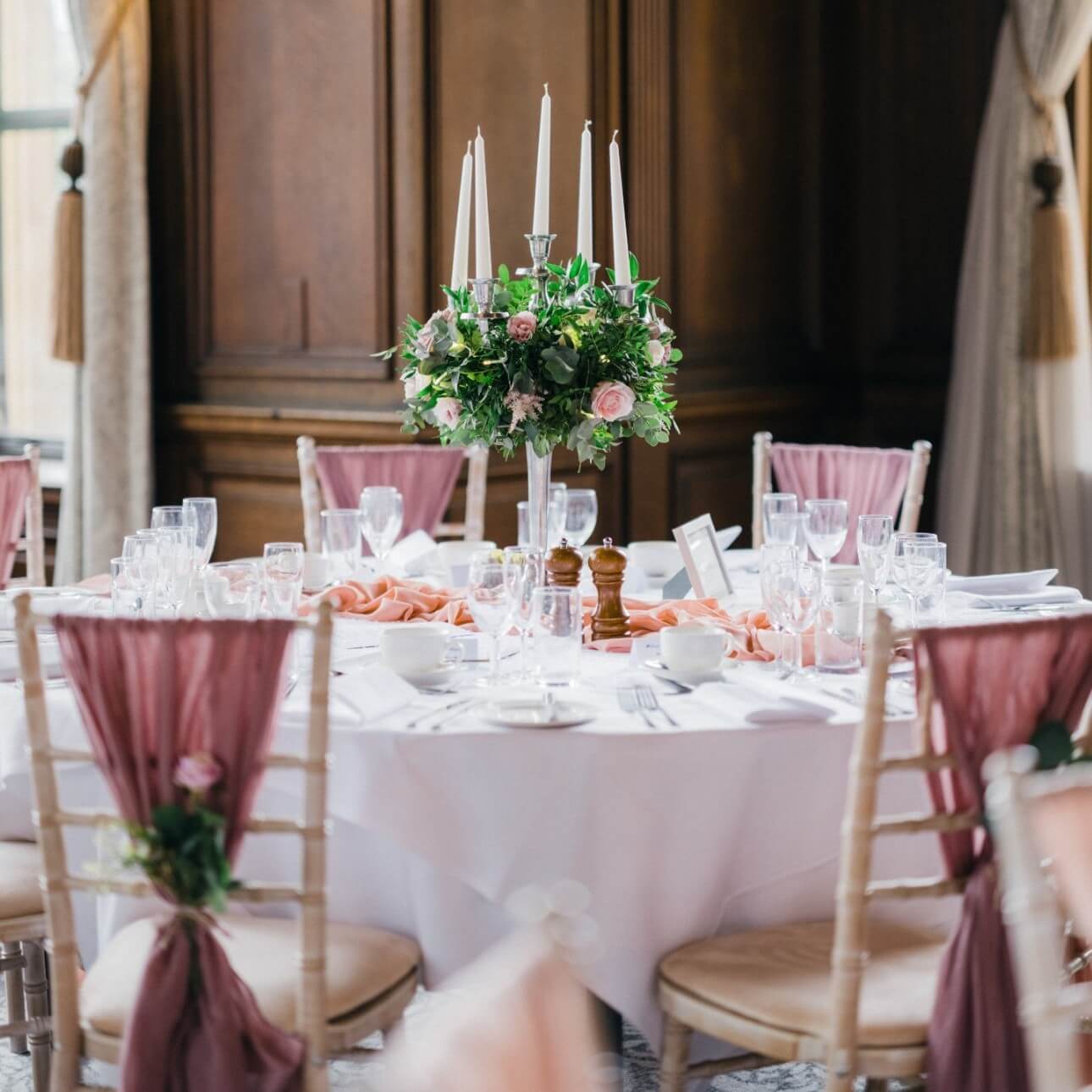 Elegant shabby chic wedding table setting with floral centrepiece, vintage-style candelabra and soft pink chair drapes.