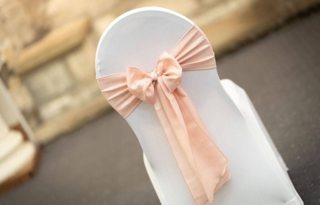 Shabby chic styling, blush pink chair sash tied into a bow on a white chair cover for romantic wedding décor.